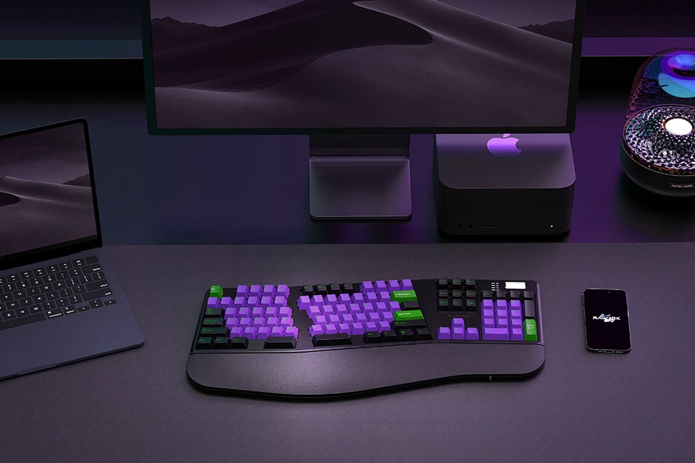 Modern computer setup with a keyboard, laptop, and phone on a dark surface.