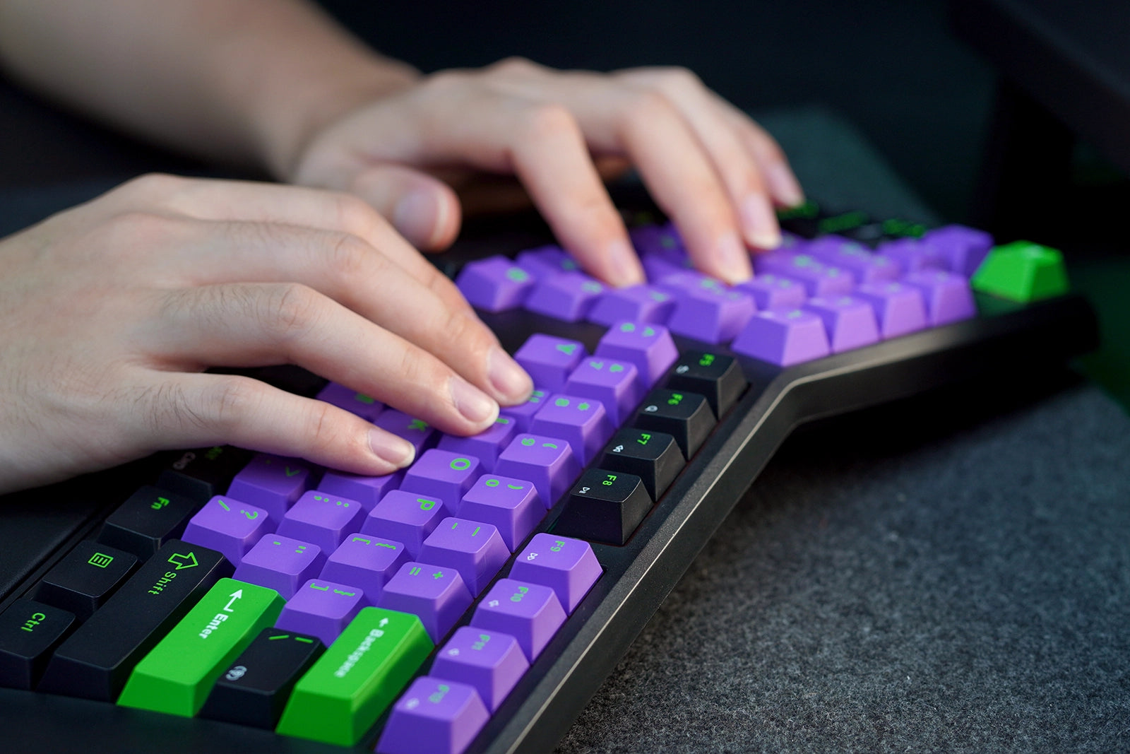 Purple and green keyboard with hands typing on a dark surface